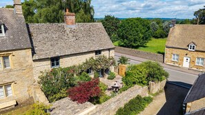 A stone cottage with a garden, a paved pathway, and a road in the background. - Rose Cottage Oddington - Countryside  Retreat, 2 bedroom, Lower Oddington (Oddington)