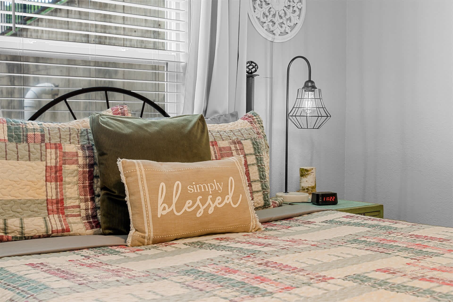 A bedroom with a bed, a bedside table, a wall clock, and a window with blinds.