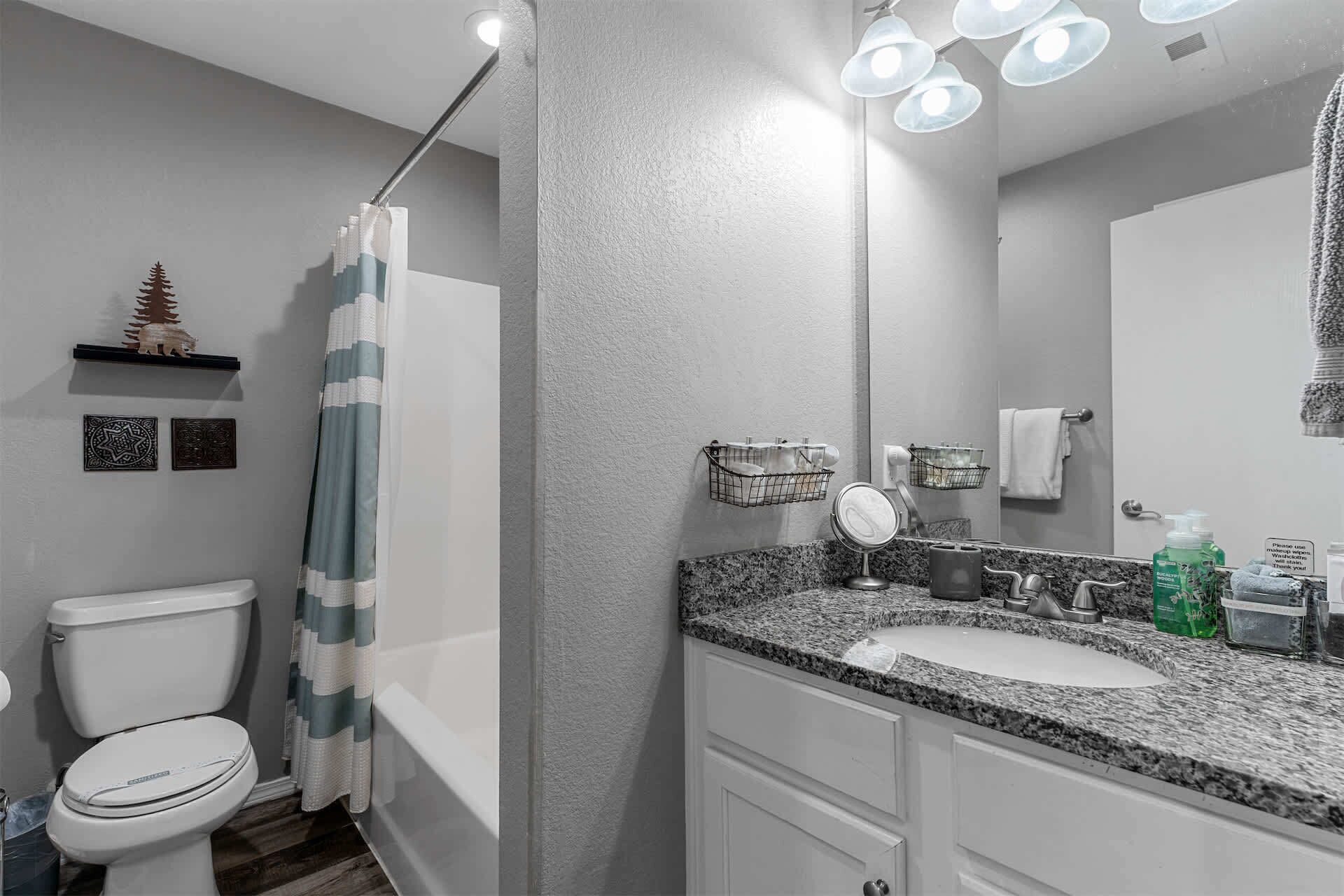 A bathroom with a toilet, shower, sink, and mirror.