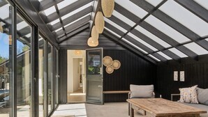 A modern loft with a sloped ceiling, large glass doors, a wooden table, a sofa, and a woven light fixture. - 4 Star Holiday Home in Rorvig (Rørvig)