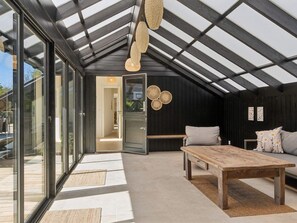 Ein modernes Loft mit geneigter Decke, großen Glasfenstern, einem Holztisch, einer Couch und einer gewobenen Leuchte.