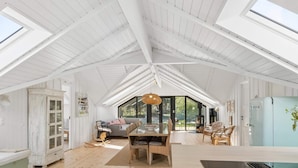 A spacious room with a high ceiling, wooden flooring, a dining area with chairs, a sofa, and a large window. - 4 Star Holiday Home in Rorvig (Rørvig)