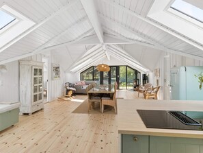 Ein geräumiger Raum mit hoher Decke, Holzboden, einer Essecke mit Stühlen, einer Couch und einem großen Fenster.