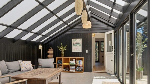 A spacious room with a high ceiling, a wooden table, a sofa, and a bookshelf. - 4 Star Holiday Home in Rorvig (Rørvig)
