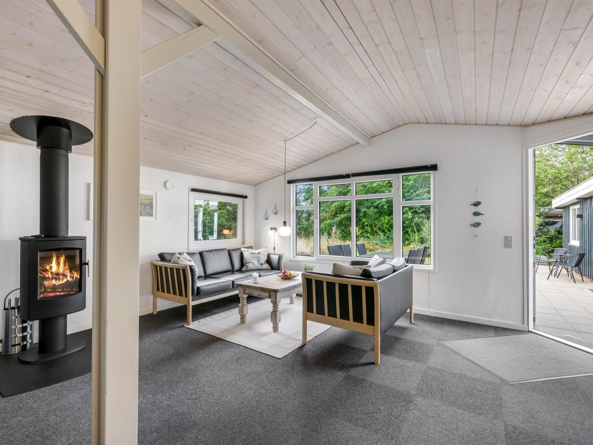 Un salon moderne avec un poêle à bois, un canapé, une table basse et une vue sur l’extérieur.