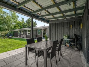 Un patio techado con mesa y sillas, una parrilla y una vista de una casa al fondo.