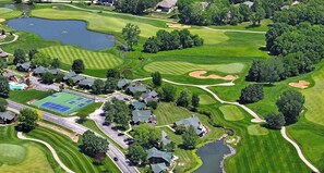 Vue aérienne d’un terrain de golf avec un court de tennis, des maisons résidentielles et un petit lac.