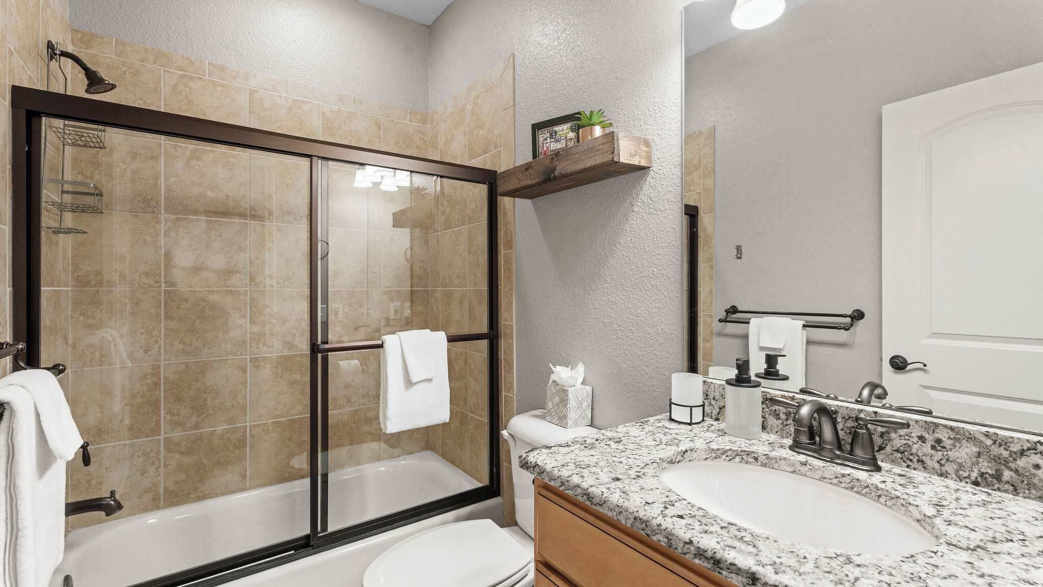 A modern bathroom with a glass-enclosed shower, a white sink, and a marble countertop.