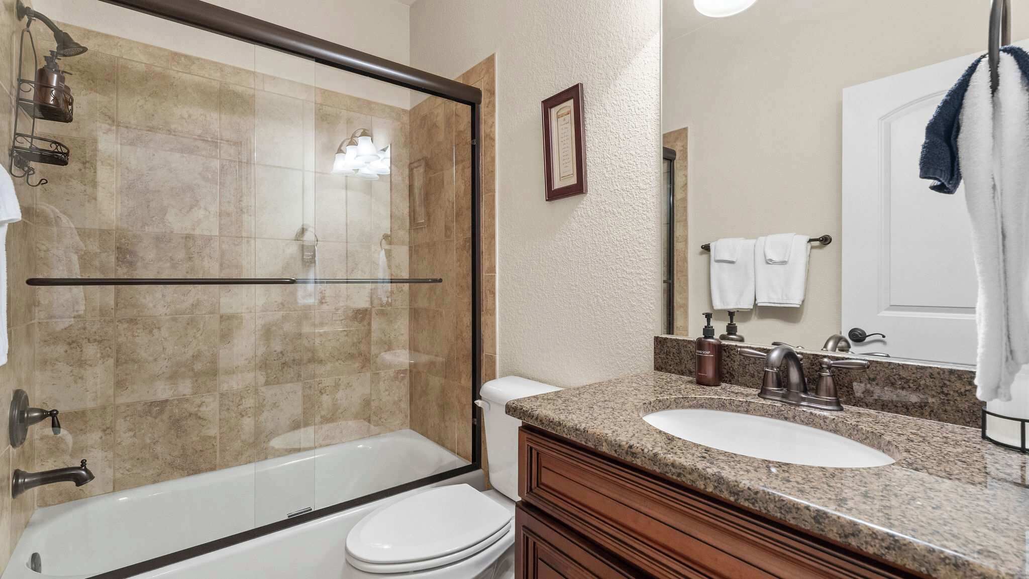 Une salle de bain avec une douche à parois de verre, des toilettes blanches, un comptoir en granit, un double lavabo et un miroir.