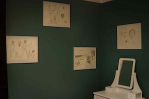 Ein Badezimmer mit grüner Wand, weißem Waschtisch und vier gerahmten Skizzen.
