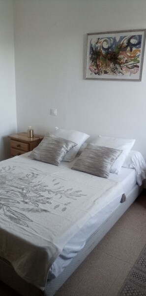 Ein Schlafzimmer mit einem Bett, Kissen, einem Nachttisch, einem Wandbild und einem Lichtschalter.