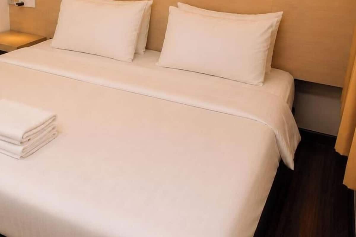 Una cama bien hecha con sábanas blancas, una toalla blanca doblada y una mesita de noche de madera con una lámpara.
