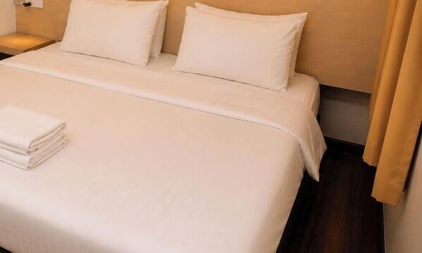 A neatly made bed with white linens, a folded white towel, and a wooden nightstand with a lamp. - H Hotel Segamat (Segamat)