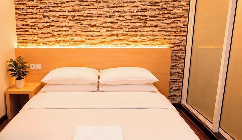 Quarto de hotel com uma cama, uma mesa de cabeceira com uma planta e uma parede com padrão de pedra.