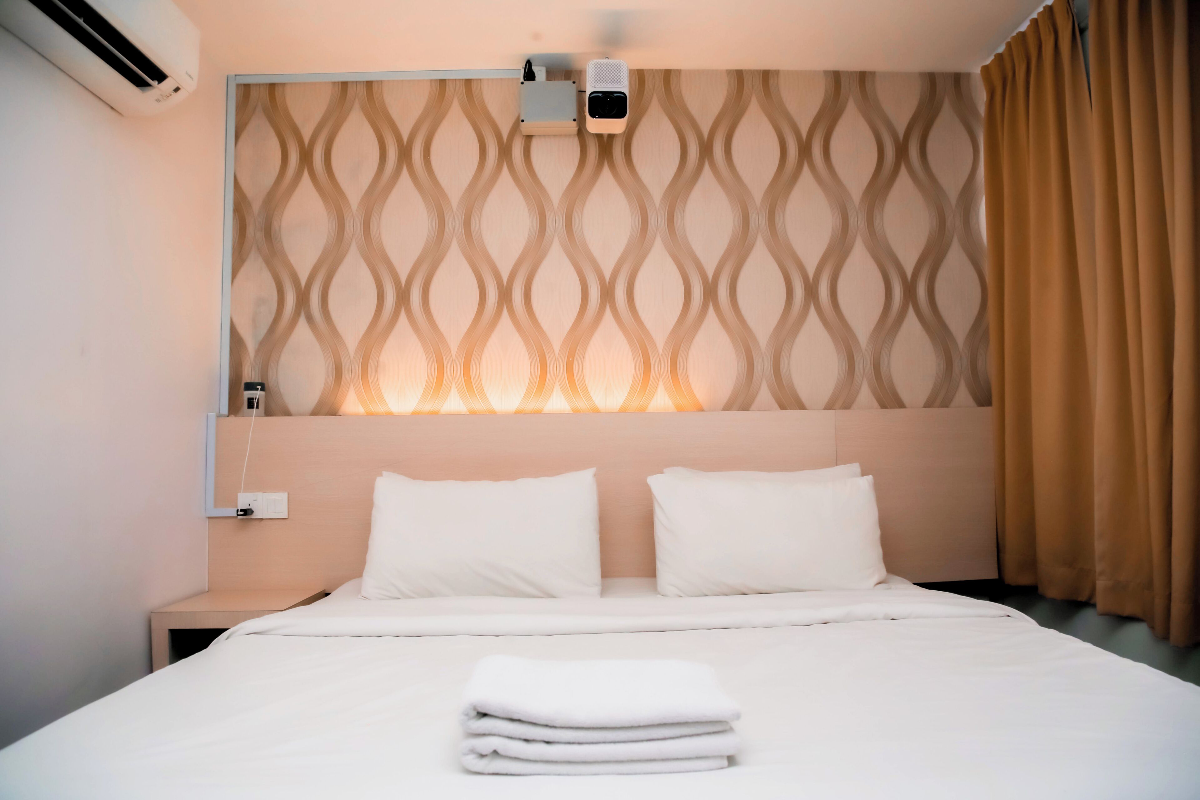 Camera d'albergo con un letto, una testiera decorata con un motivo a fantasia, un condizionatore d'aria e un comodino.