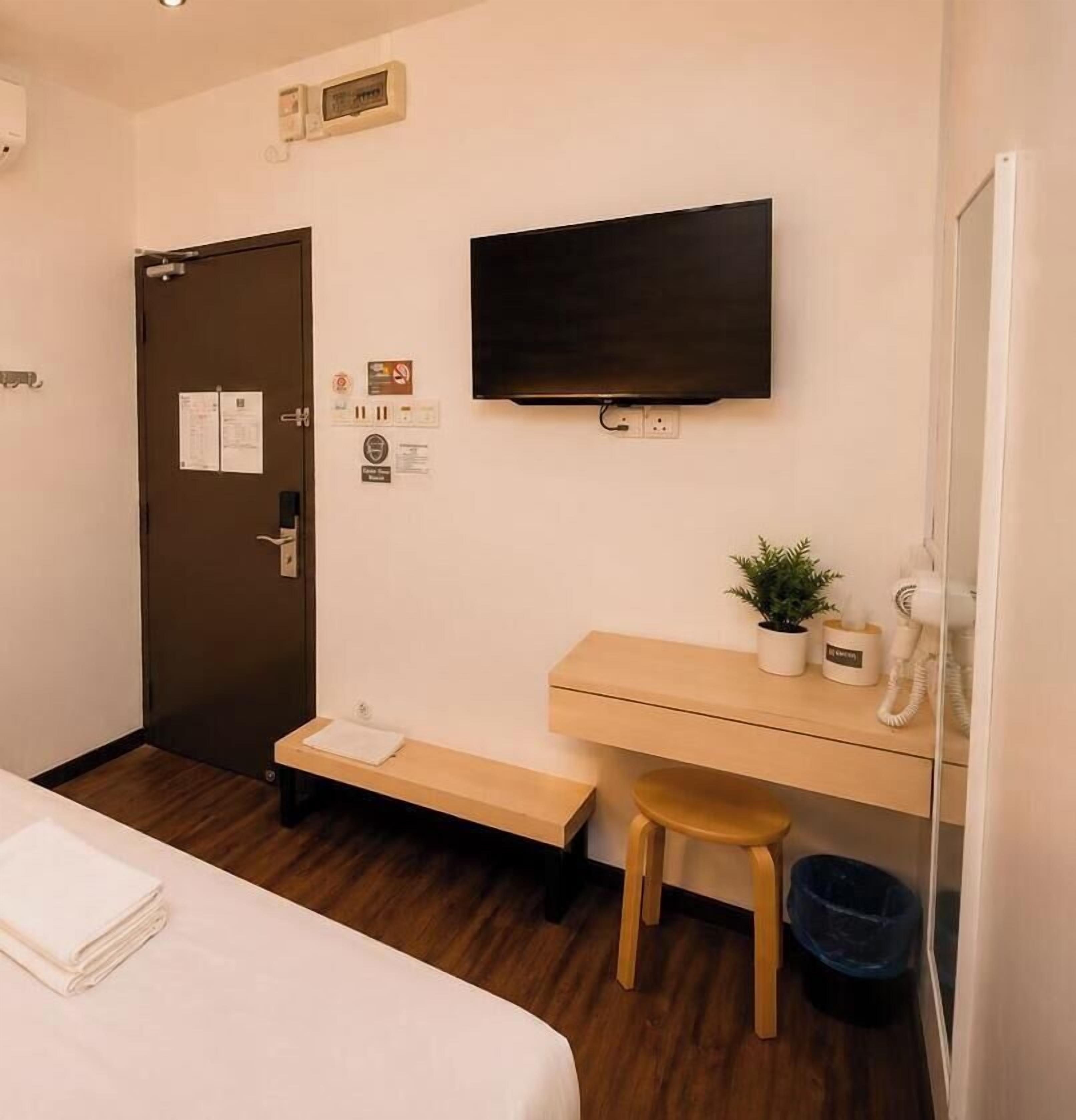 A hotel room with a bed, a desk, a television, a telephone, and a small plant.