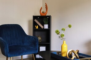 A blue armchair, a black bookshelf with decorative items, and a yellow vase with green flowers.
