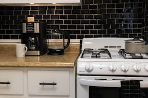 A kitchen with a gas stove, a coffee maker, and a kettle.