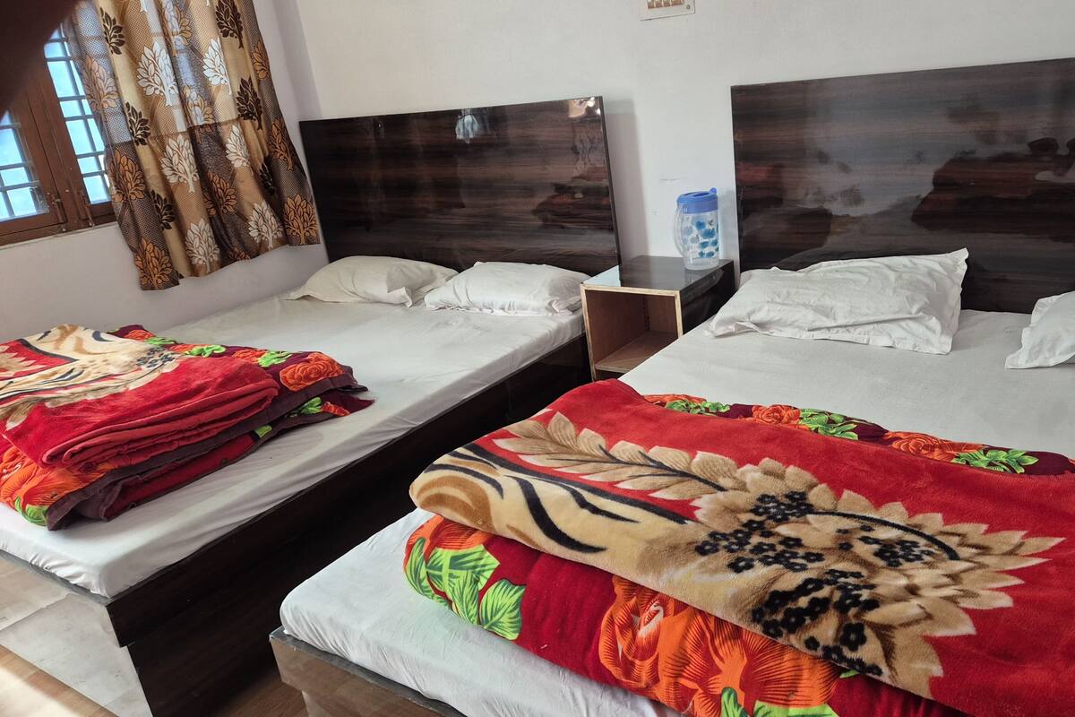 Two single beds with white linens and floral-patterned blankets, a wooden nightstand, and a window with patterned curtains.