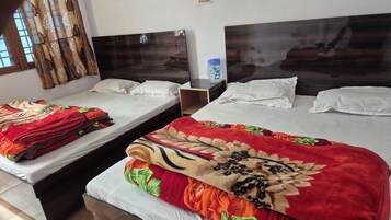 Two single beds with white linens and floral-patterned blankets, a wooden nightstand, and a window with patterned curtains.
