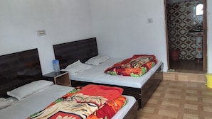 Een hotelkamer met twee bedden, een plafondventilator, een badkamer zichtbaar door een geopende deur, en een houten vloer met een herringbone-patroon.