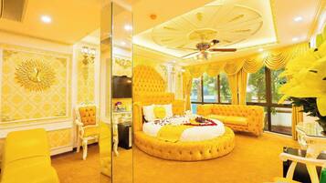 A luxurious room with a round bed, a mirror, a sofa, and a dining table.