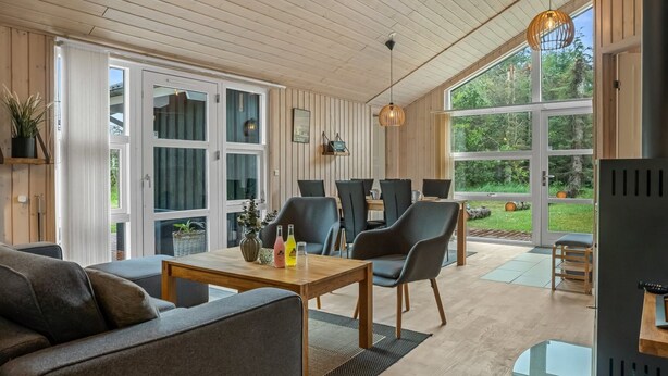 Ein modernes Interieur mit Holzboden, großen Fenstern, einer Essecke mit Stühlen und einem Sofa.