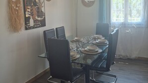 Een eetruimte met een glazen tafel, zwarte stoelen, een wandlamp en een raam met gordijnen.