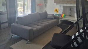 Een moderne woonkamer met een grijze bank, een zwarte stoel, een klein tafeltje met decoratieve items en uitzicht op het buitenleven door een raam.