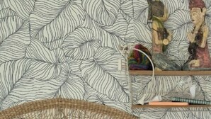 Een bed met een geweven hoofdbord, een kussen met een flamingo-design en een behang met patroon.