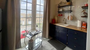 A kitchen with a large window, a sink, cabinets, and a shelf with kitchenware. - Shelby by the Seashore C1 (Galveston)