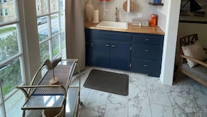 A modern kitchen with a large window, a sink, and blue cabinets. - Shelby by the Seashore C1 (Galveston)