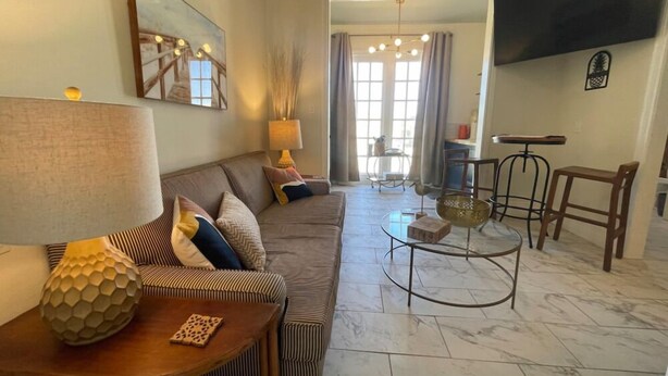 A living room with a sofa, a coffee table, and a TV mounted on the wall. - Shelby by the Seashore C1 (Galveston)