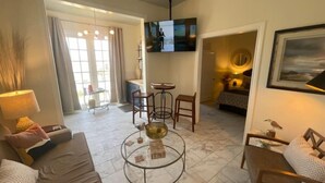 A living room with a sofa, coffee table, TV, and a dining area with chairs and a table. - Shelby by the Seashore C1 (Galveston)