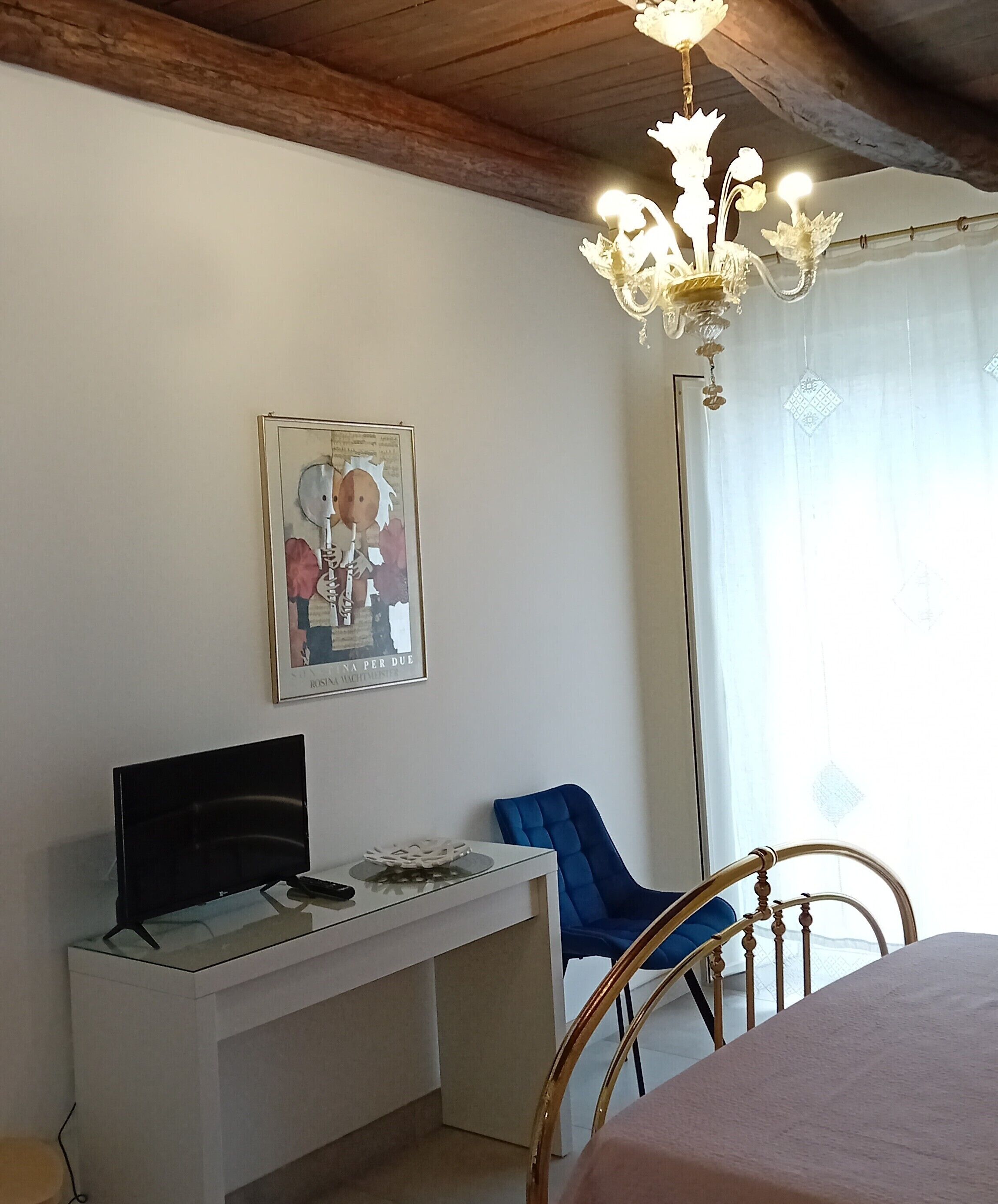 A room with a desk, a television, a blue chair, a bed, and a chandelier.