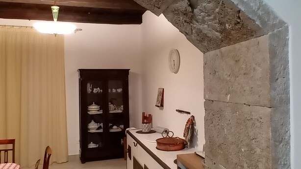 A kitchen with a stone archway, wooden ceiling beams, a dining table with chairs, and a cabinet with dishes. - B&B Sotto il Figliolo - The perfect starting point for exploring the Alburni Mountains (Petina)