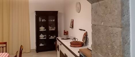 Une cuisine dotée d’une arche en pierre, de poutres en bois au plafond, d’une table à manger avec des chaises et d’un buffet contenant de la vaisselle.
