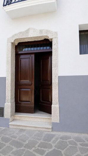 Eine doppelte Holztür mit Steinrahm, ein kleines Fenster darüber und ein gepflasterter Grund aus Stein.