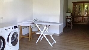 A laundry area with a washing machine, ironing board, and wooden flooring.