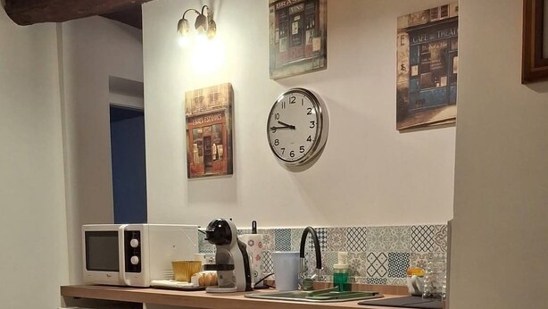 A compact kitchen with a microwave, kettle, and a clock on the wall.