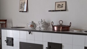 A kitchen with white tiles, a copper pot, a teapot, and two framed pictures on the wall.
