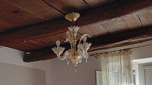 A bedroom with a bed, a chandelier, a window with curtains, and a wooden ceiling.