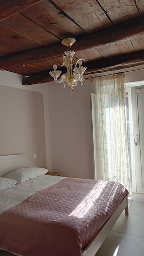 A bedroom with a bed, a chandelier, a window with curtains, and a wooden ceiling. - B&B Sotto il Figliolo - The perfect starting point for exploring the Alburni Mountains (Petina)