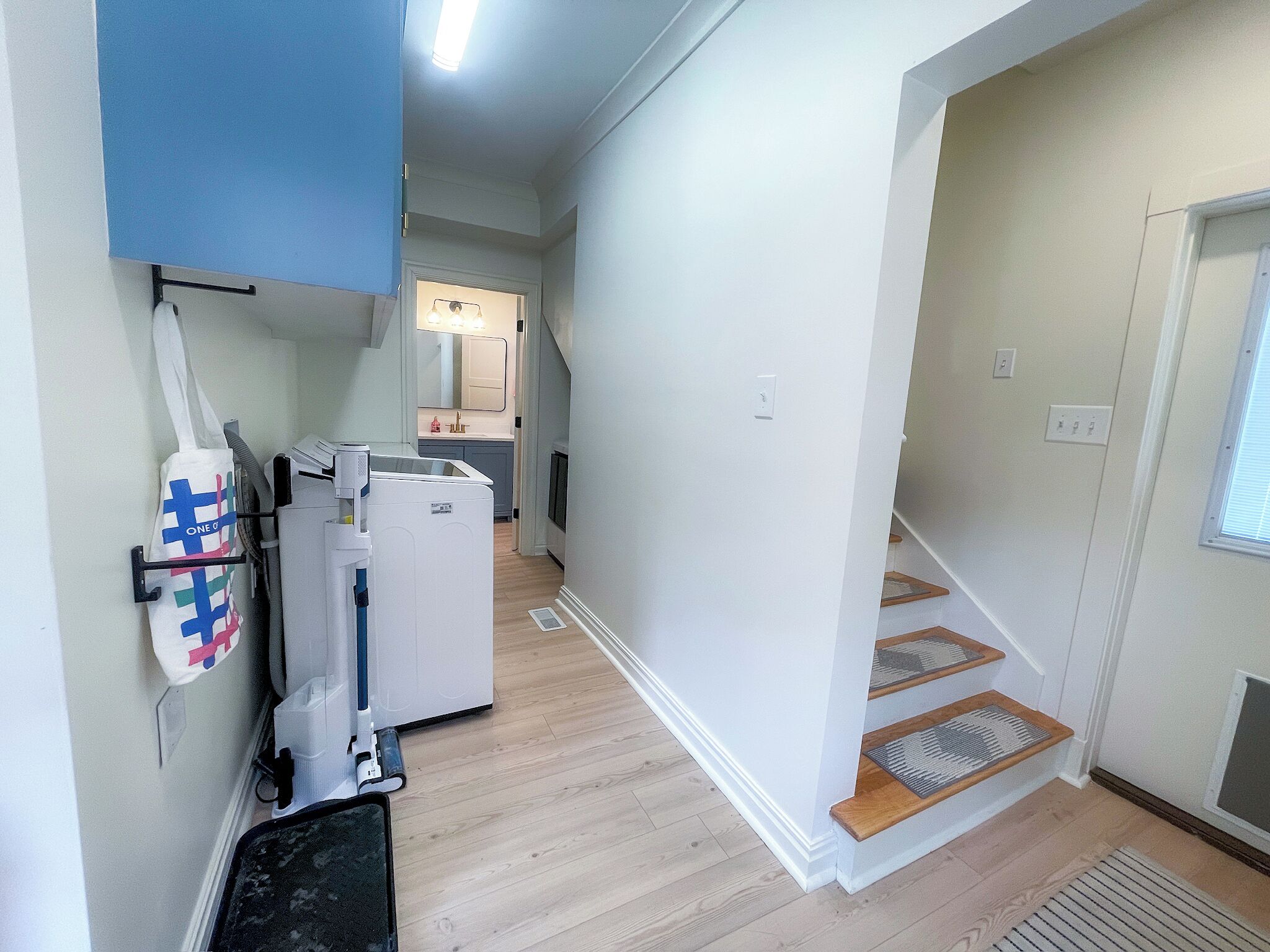 Um corredor com uma máquina de lavar roupa, um varal e uma escadaria que dá para outro quarto.