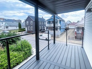 Eine Holzterrasse mit Metallgeländer, die auf eine Wohnstraße mit Häusern und geparkten Autos blickt.
