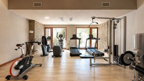 Un gimnasio con equipo de ejercicio, pared de piedra y ventanas grandes.