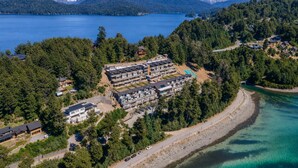 An aerial view of a coastal resort with multiple buildings, a swimming pool, and a road leading to the beach.