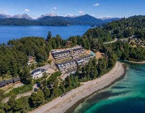 An aerial view of a coastal resort with multiple buildings, a swimming pool, and a road leading to the beach. - Blue Aparts Angostura (Villa La Angostura)