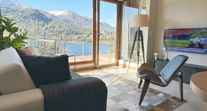 Una sala de estar moderna con un sofá, un sillón, un televisor y vistas a un lago y montañas.