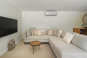 A living room with a large flat-screen TV, a beige sectional sofa, a small round coffee table, and two wall-mounted lanterns. - Spacious 4-bedroom house with AC in marvelous Playa Langosta (Playa Langosta)